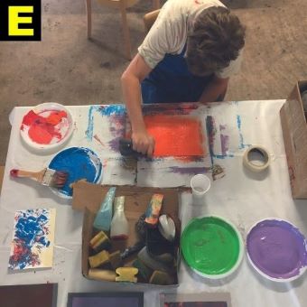 ein Künstler im Atelier umgeben von Farbtuben, aufgenommen von oben.