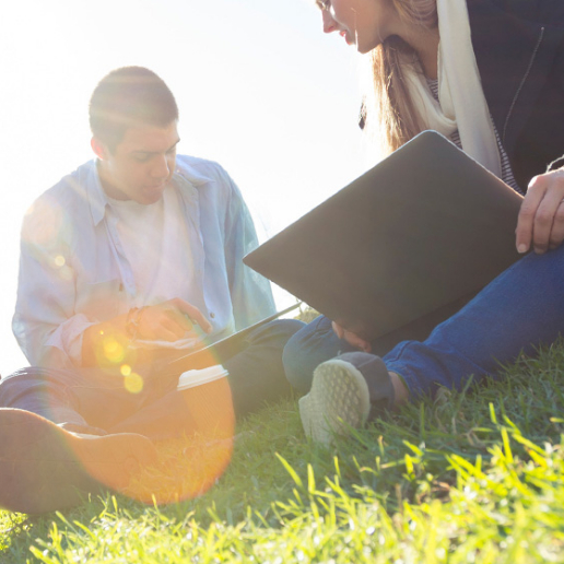 zwei Personen sitzen in einer Wiese mit Laptop und Tablet 