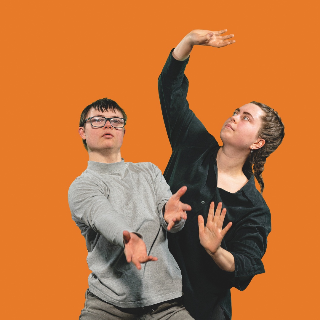 Zwei junge Menschen in ausdrucksstarker Pose vor orangem Hintergrund.