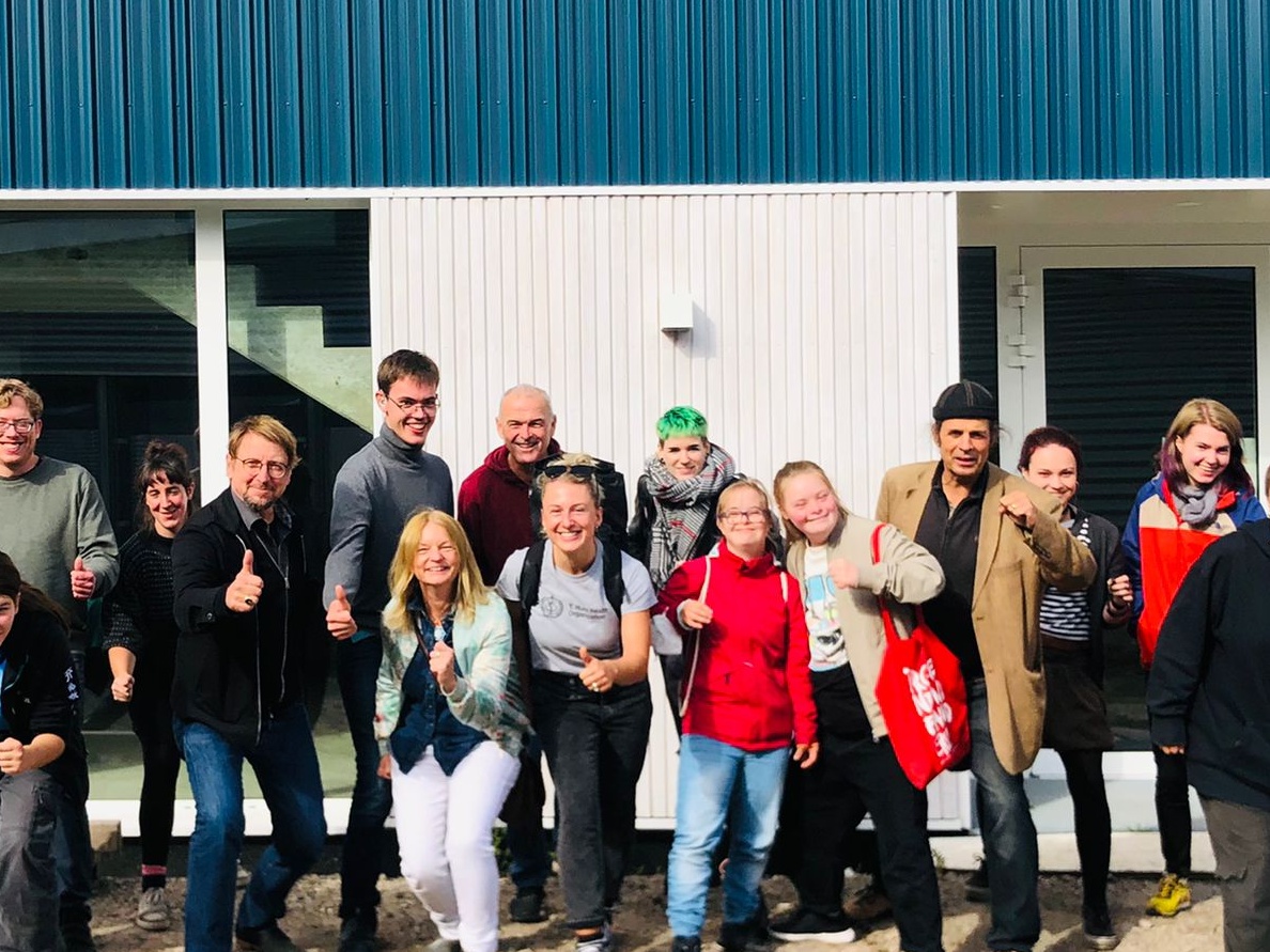 Gruppenfoto. Überwiegend glückliche Gesichter, hochgestreckte Daumen. Viele gehen einen Schritt auf die Kamera zu.