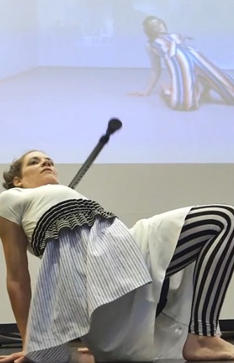 tanzende Person auf Knien mit Krücke, im Hintergrund eine animierte Projektion von ihr
